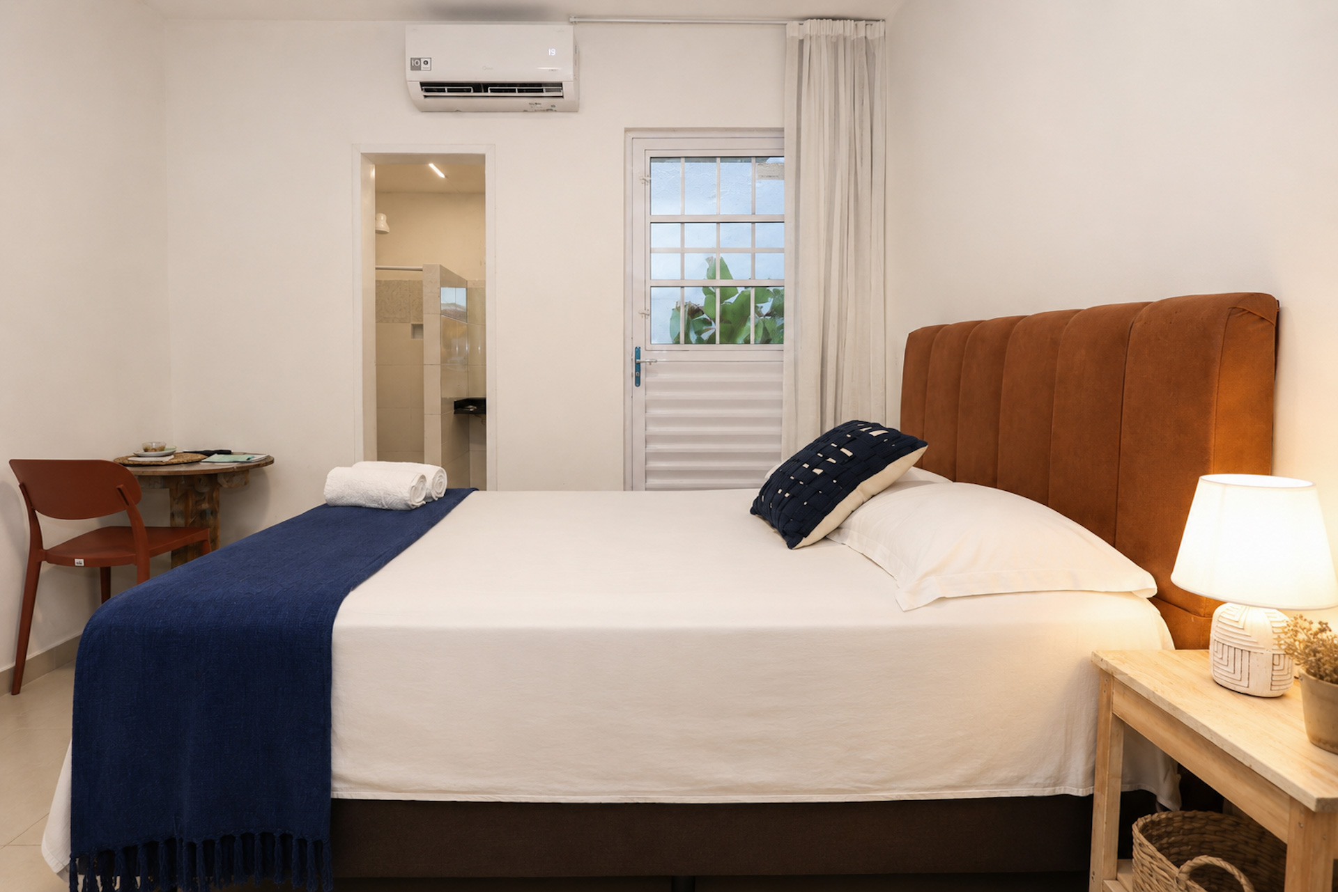 Quarto de casal com manta azul-marinho e porta para varanda ao fundo